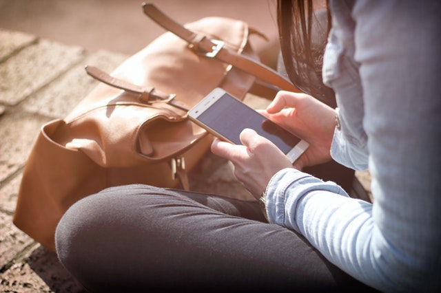 Dívka sedící na zemi, držící telefon v ruce